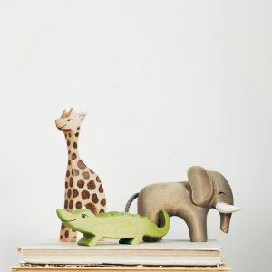 A close-up of wooden giraffe, elephant, and crocodile figurines stacked on books.